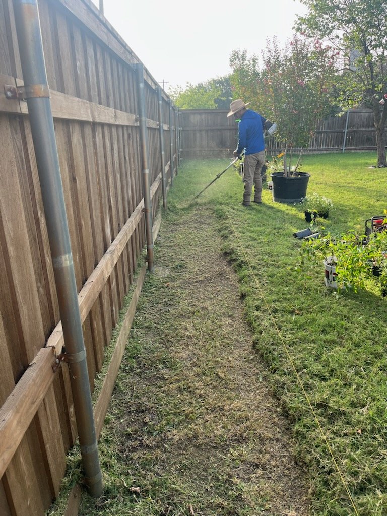 Worker trimming grass along a wooden fence